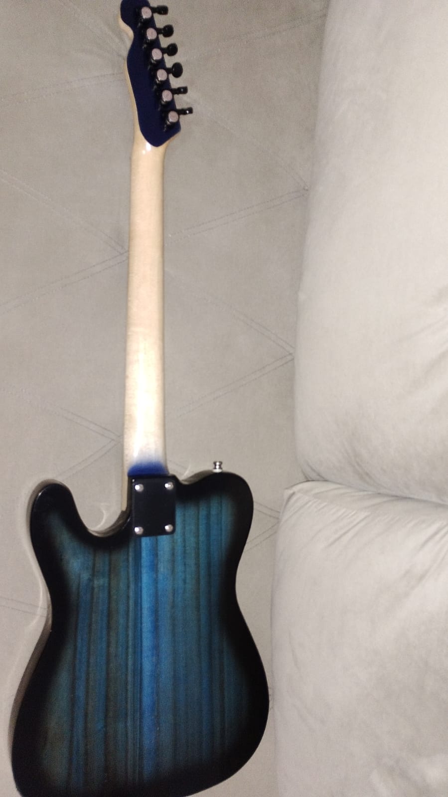 Vista traseira da guitarra azul e preta apoiada no sofá, mostrando o encaixe do braço